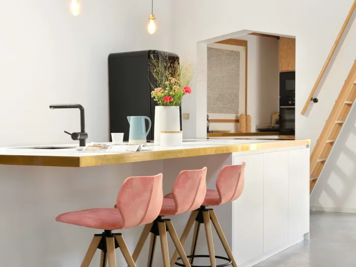 Moderne Küche mit weißen Schränken, rosa Barhockern und Blumendekoration auf der Kücheninsel