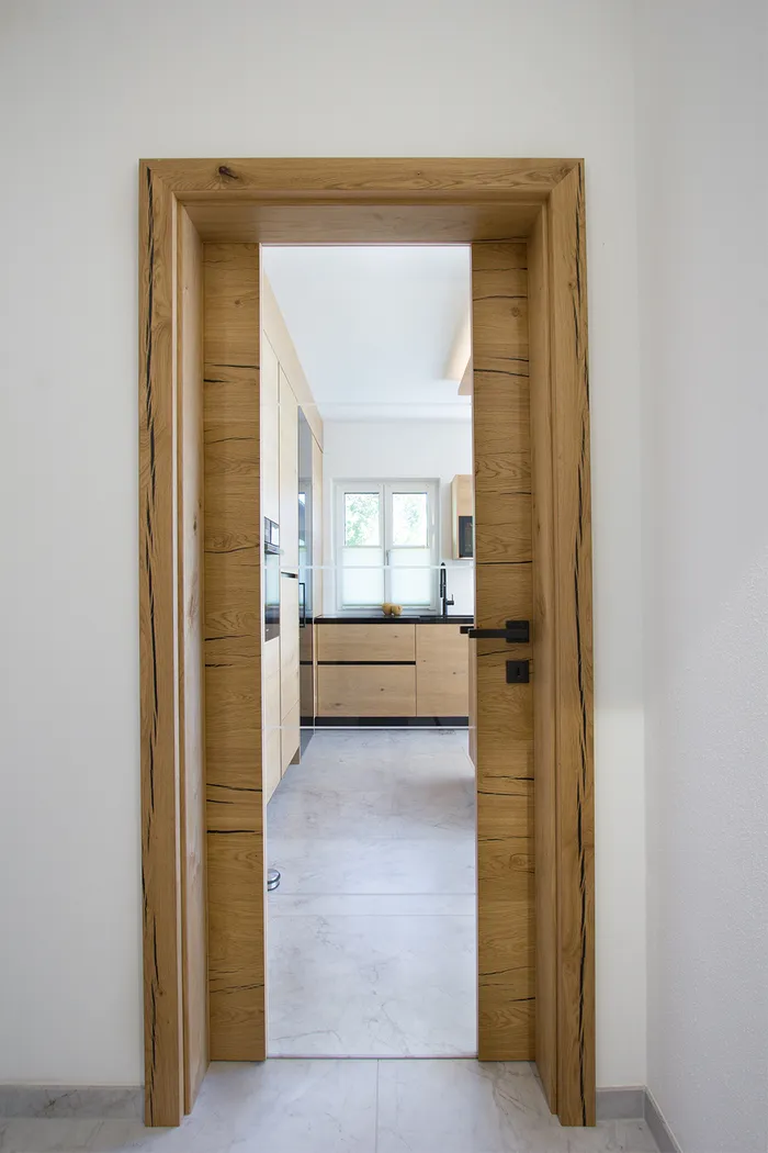 Moderne Küche mit Holzfronten und Marmorfliesen durch Holztürrahmen sichtbar