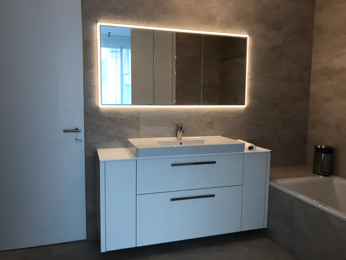 Modernes Badezimmer mit LED-beleuchtetem Spiegel und weißem Waschtisch neben Badewanne