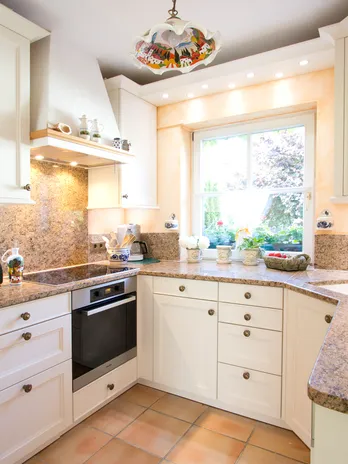 Landhausküche klasisch mit Granit-Arbeitsplatten, weißen Schränken und Blick auf Garten durch Fenster