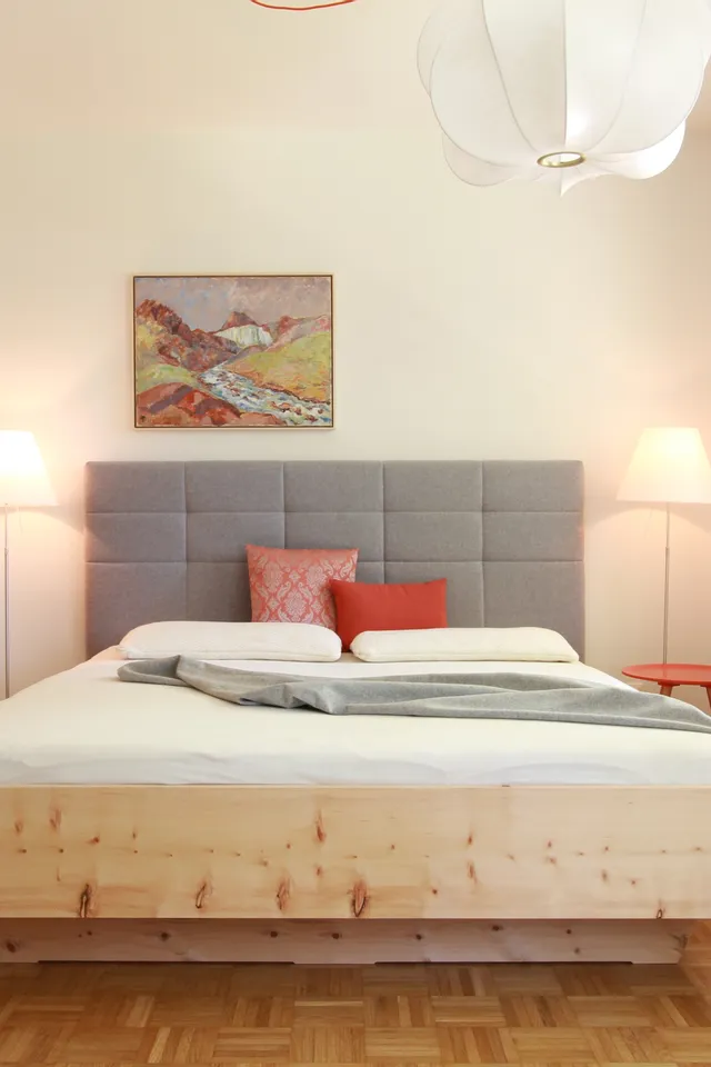 Modernes Schlafzimmer mit grauem Polsterbett, Holzmöbeln und dezenter Beleuchtung