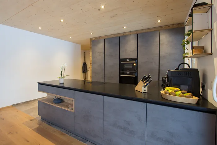 Moderne Küche mit grauen Fronten, schwarzer Arbeitsplatte und integrierten Geräten