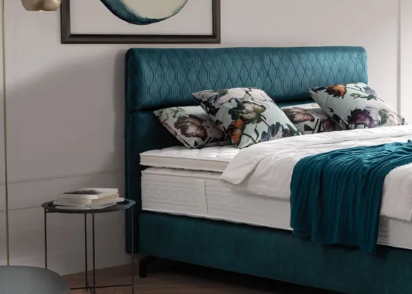 Modernes Boxspringbett mit türkisfarbenem Polster und floral dekorierten Kissen in hellem Schlafzimmer