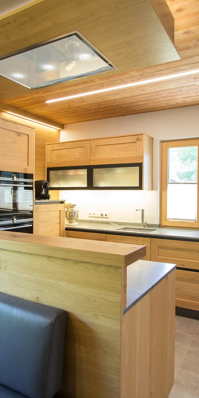 Moderne Küche mit Holzschränken, schwarzem Sofa und großen Fenstern im natürlichen Licht