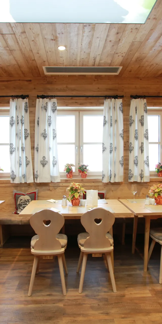 Gemütliches Restaurant mit Holzwänden, dekorierten Tischen und weißen Vorhängen im Alpenstil