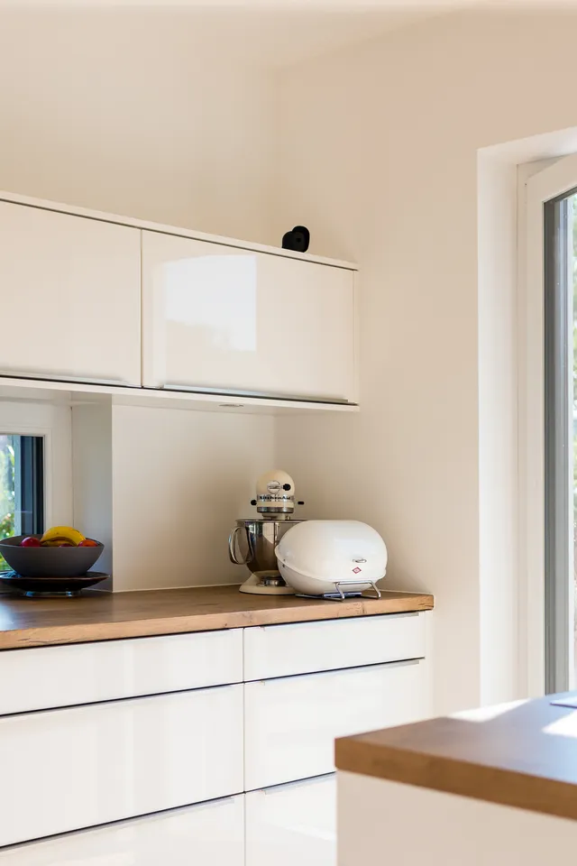 Moderne weiße Küche mit Holzarbeitsplatte und Blick in einen sonnigen Garten