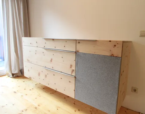 Moderne Hängeschrankkommode aus hellem Holz mit grauer Stofftür in minimalistischem Raum