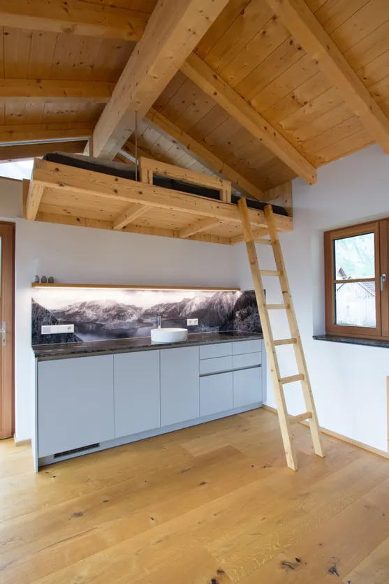 Moderne Küchenzeile mit Holzleiter zu einem Hochbett unter einem Dach aus Naturholz