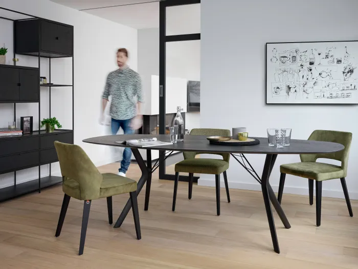 Modernes Esszimmer mit ovalem Tisch, grünen Stühlen und schwarzem Regal auf hellem Holzboden