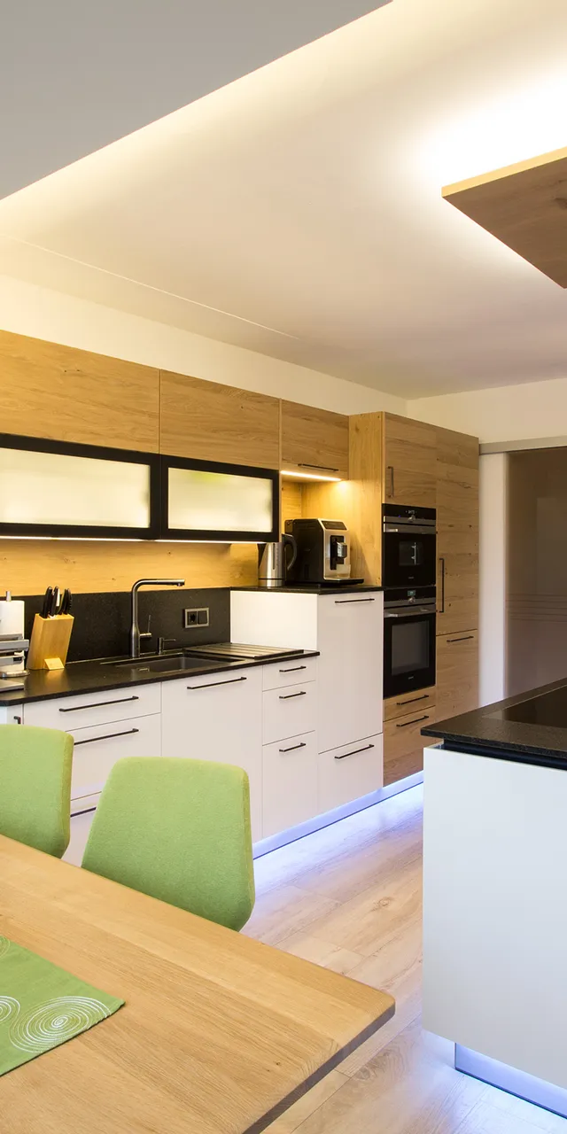 Moderne Küche mit Holzfronten, schwarzer Arbeitsplatte und LED-Beleuchtung unter Schränken