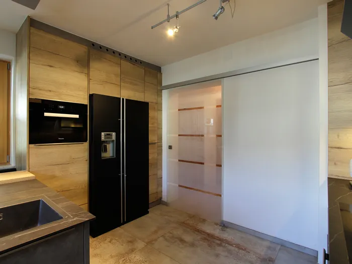 Moderne Küche mit schwarzen Einbaugeräten, Holzverkleidung und Glasschiebetür