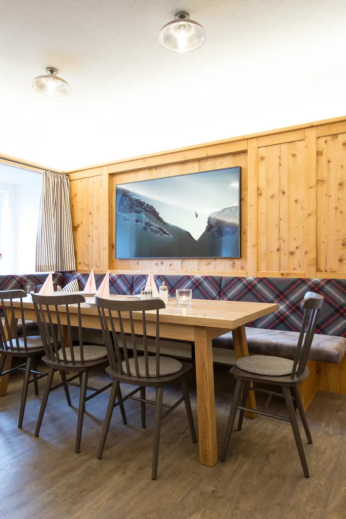 Gemütlicher Essbereich mit Holzmöbeln, kariertem Polster und Bergbild an der Wand
