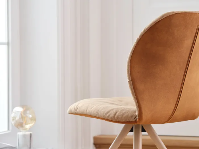 Moderner Stuhl mit beiger Sitzfläche und Holzbeinen in hellem, minimalistischem Raum