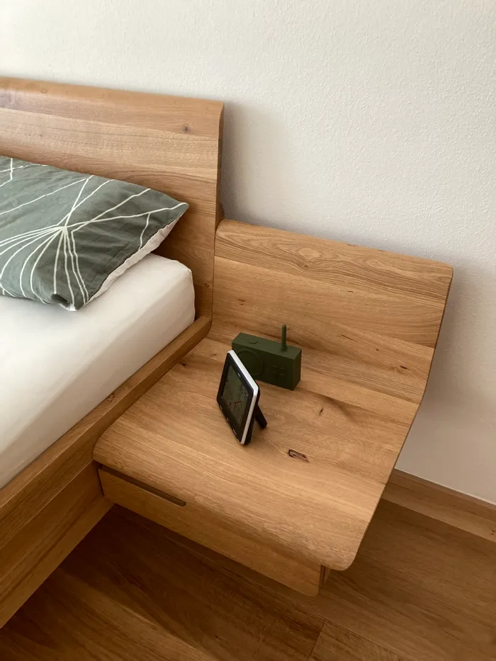 Holznachttisch mit grünem Radio und GPS-Gerät neben Bett mit grün gemustertem Kissen