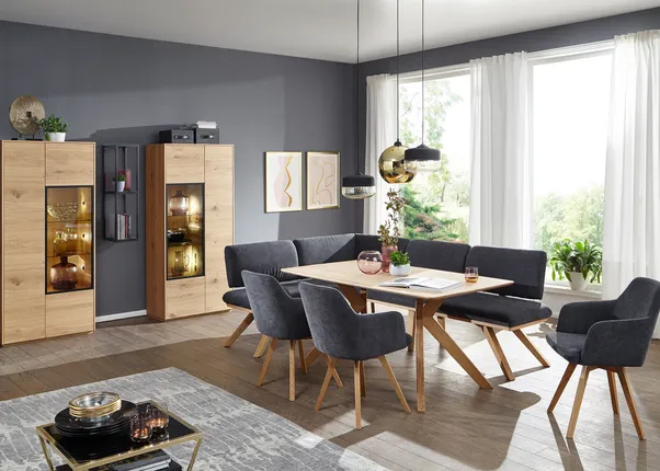 Moderne Esszimmermöbel aus Holz mit grauen Polsterstühlen und Vitrine vor grauer Wand