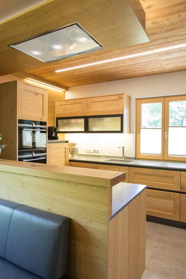 Moderne Küche mit Holzschränken, schwarzem Sofa und großen Fenstern im natürlichen Licht