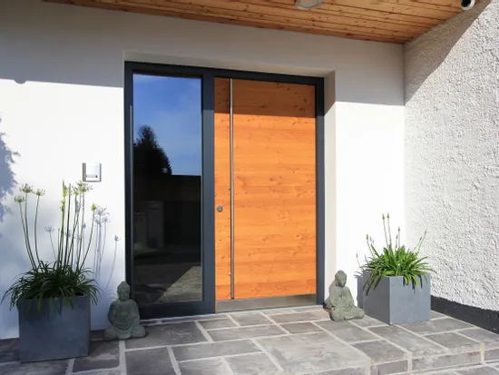 Moderne Hauseingangstür aus Holz mit Glasseite, Fliesenboden und Pflanzkübeln mit Buddhafiguren