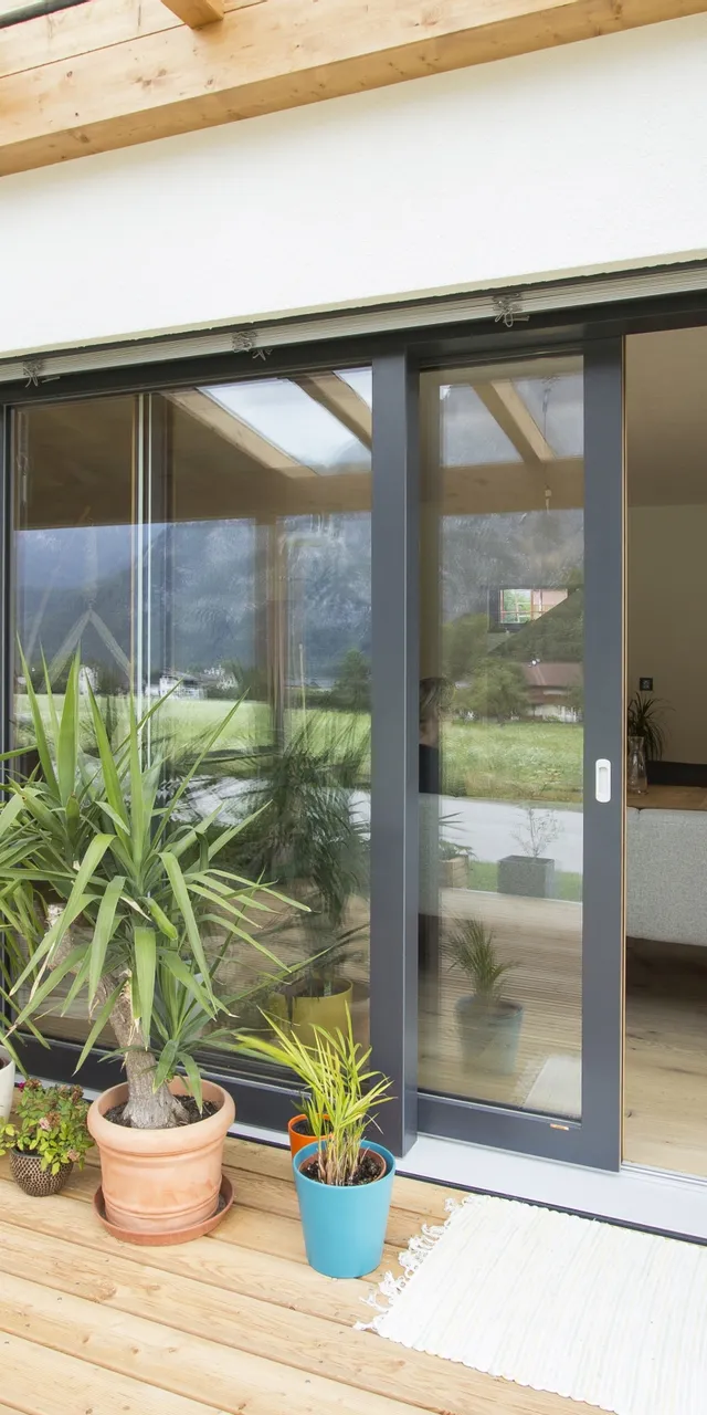 Moderne Terrasse mit Holzboden, grünen Liegestühlen und Pflanzen vor großer Glasschiebetür
