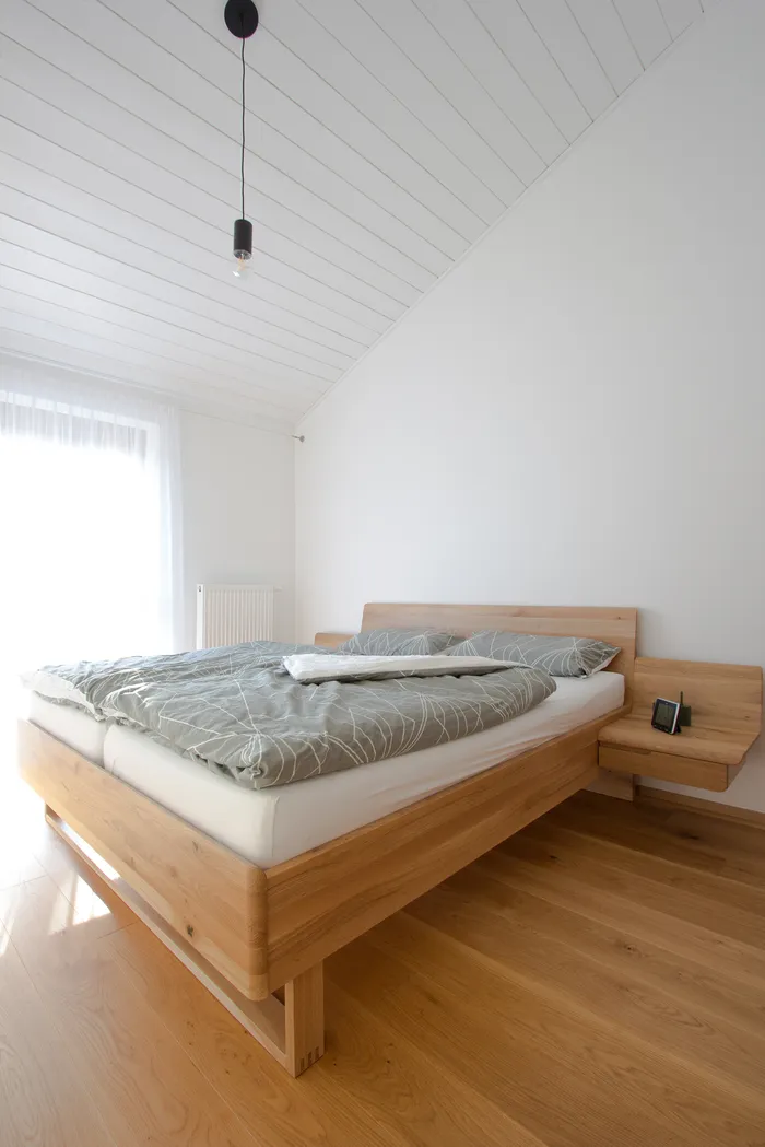 Modernes Schlafzimmer mit Holzbett, grauer Bettwäsche und natürlichem Licht durch ein Fenster