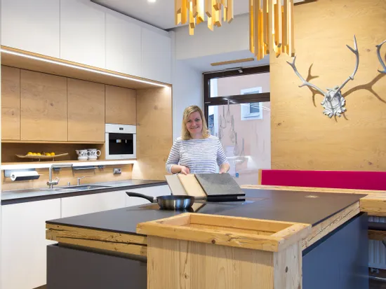 Moderne Holzküche mit Kochinsel, stilvollen Hängelampen und Frau mit Musterplatten