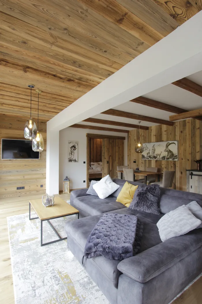 Modernes Wohnzimmer mit grauem Sofa, Holzwänden und dekorativem Essbereich in Alpenstil